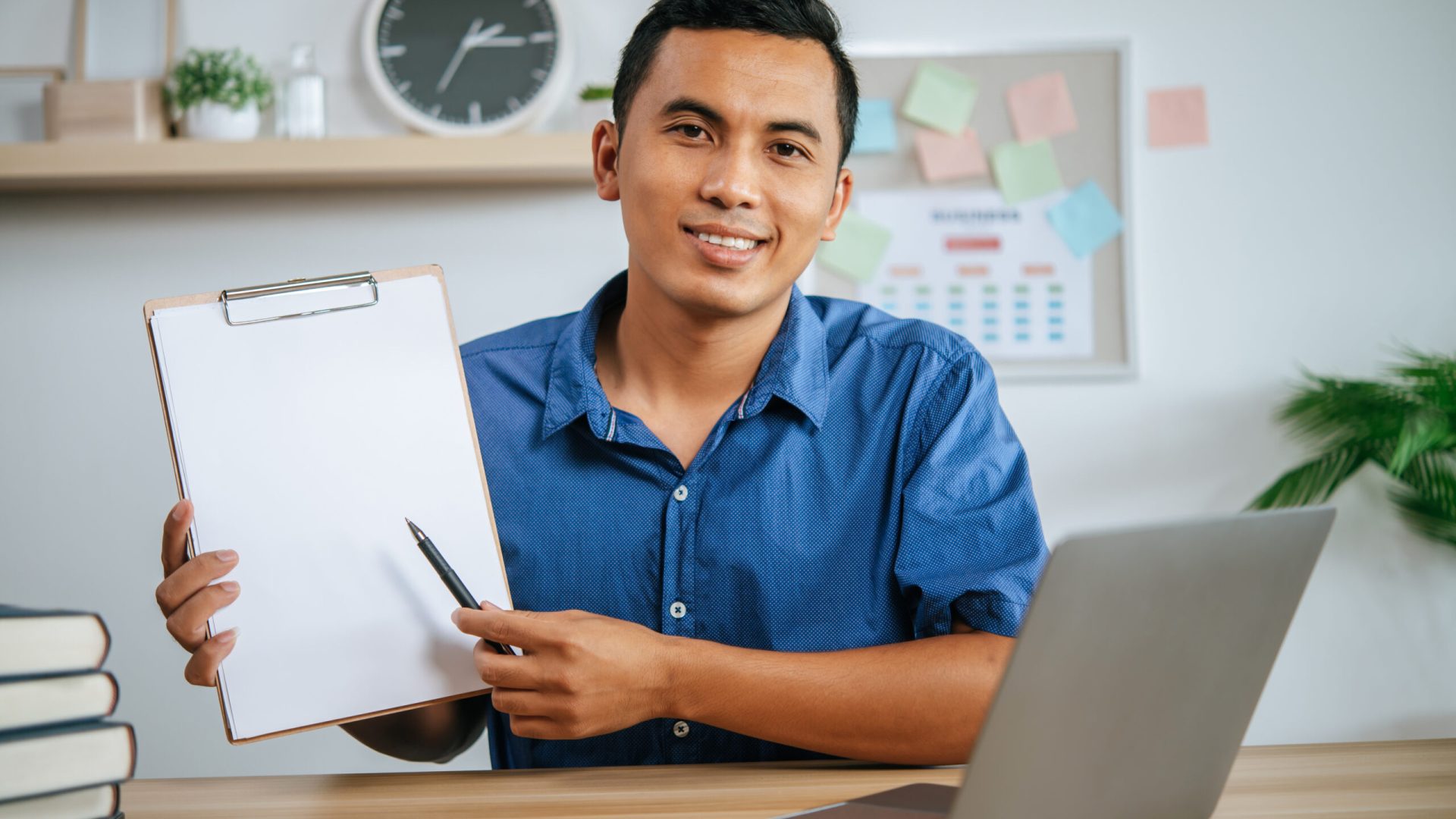 man working in office holding papers with laptop on desk